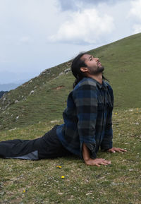 A long haired handsome indian young man doing cobra pose, bhujangasana yoga pose in the mountain 
