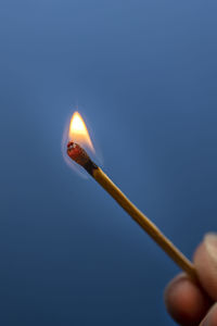 Close-up of hand holding lit matchstick against blue background