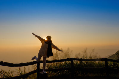Portrait of smiling woman with arms outstretched standing against sky during sunrise