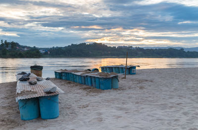 Deck chairs on beach against sky during sunset