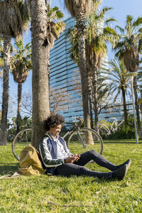 Casual businessman with bicycle using cell phone in urban park, barcelona, spain