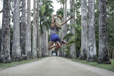 Woman jumping on road amidst tree trunk