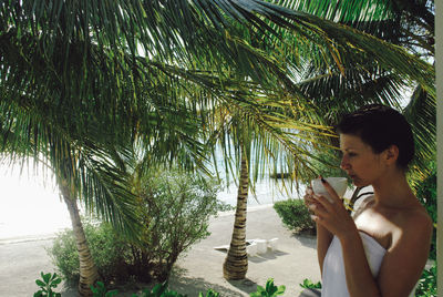 Young woman looking away while standing on palm tree