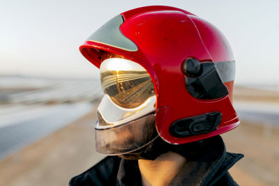 Unrecognizable firefighter wearing protective hardhat and special uniform with yellow reflective patches on background of clear sky in daytime