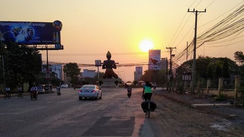People riding motorcycle on road against sky during sunset