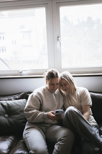 Homosexual couple sitting on sofa and using cell phone