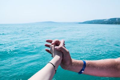 Cropped image of people holding hands against sea