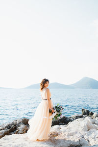 Woman standing on rock by sea against sky