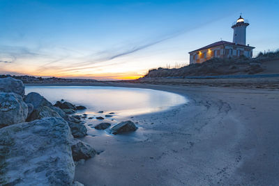 Lighthouse by sea against sky during sunset