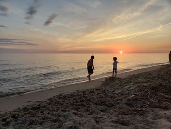 Siblings at beach against sky during sunset