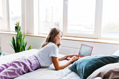 Side view of woman sitting on bed at home