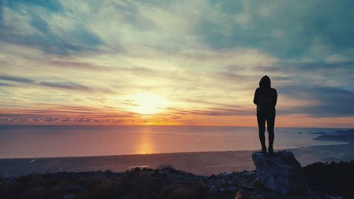 Silhouette woman standing on rock at beach against sky during sunset