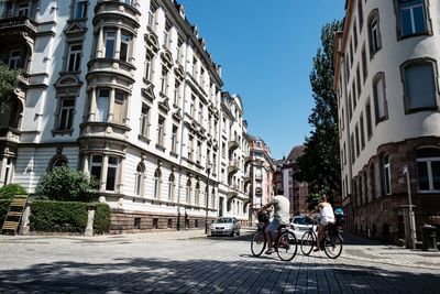 People riding bicycle on street amidst buildings in city