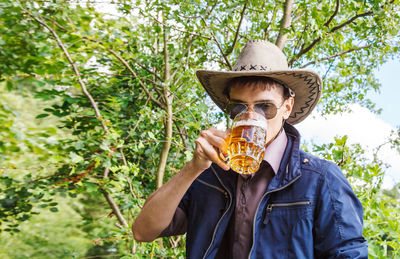 Portrait of man drinking beer against tree
