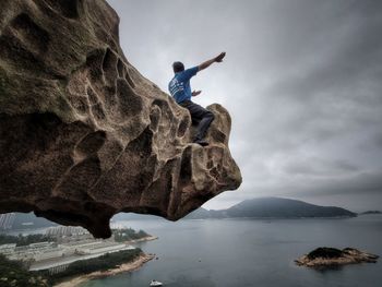 Man standing on rock by sea against sky