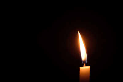 Close-up of burning candle against black background