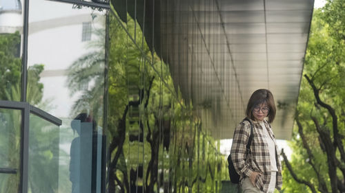 Portrait of young woman standing against window wall