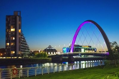 Illuminated bridge over river against buildings in city