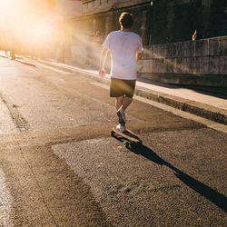 Rear view of a skateboarder in city sunflare