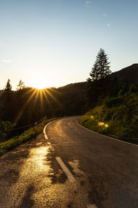 Road amidst trees against sky during sunset