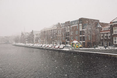 River by buildings against sky during snowfall