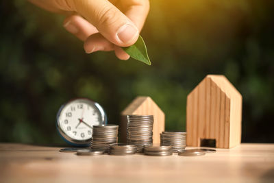 Close-up of hand holding leaf over coins and model house on table