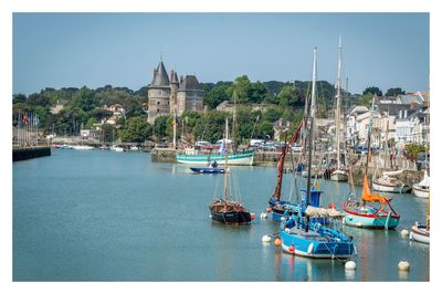 Sailboats moored in harbor by buildings against sky