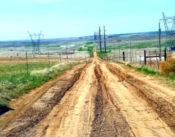 Dirt road amidst field against sky