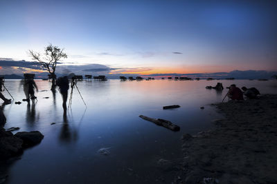 Silhouette man and woman photographing sea during sunset