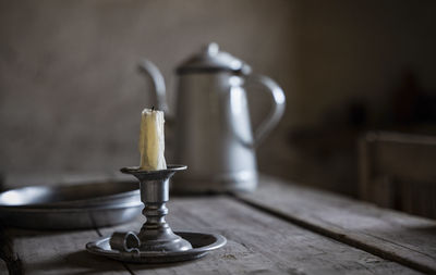 Close-up of old candlestick holder, plates and water jar on wooden table