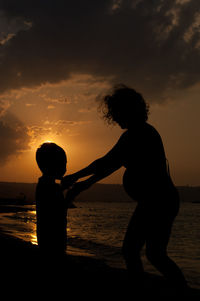Silhouette friends standing on shore against sky during sunset