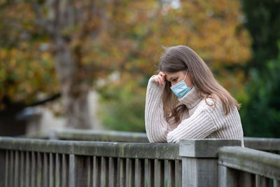 Woman sitting on railing at park during autumn