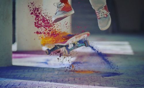 Low section of man performing stunt while powder paint splashing from skateboard
