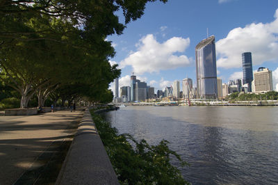 City by river and buildings against sky