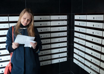 Young woman reading letter by mailbox