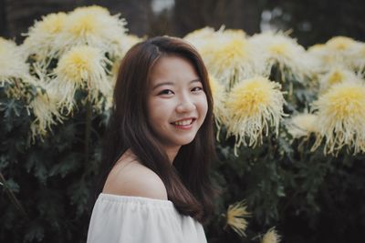 Portrait of smiling young woman by plants at public park