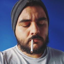 Close-up of man with cigarette against blue background