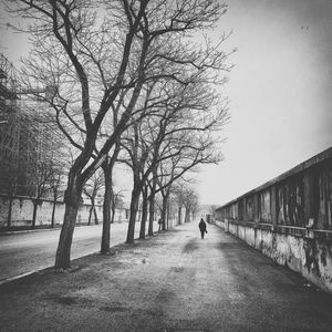 Person walking on sidewalk by wall against sky