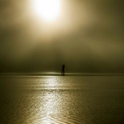 Silhouette person standing in sea against sky during sunset