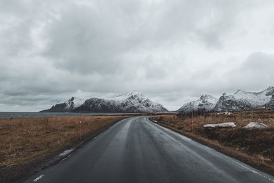 Road leading towards snowcapped mountains against sky