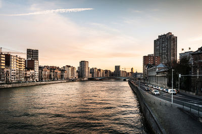 River amidst buildings in city against sky during sunset