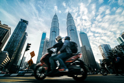 Low angle view of people riding motorcycle on street against petronas towers