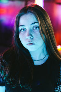 Close-up portrait of beautiful young woman against illuminated lights