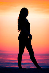 Silhouette woman standing at beach against sky during sunset