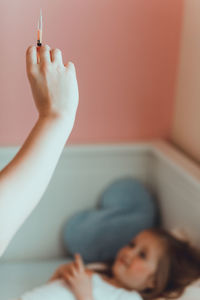 Cropped hand of mother holding syringe with daughter on bed at home