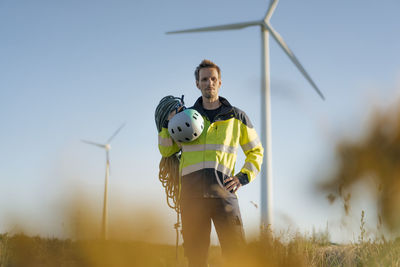 Technician standing in a field at a wind farm with climbing equipment