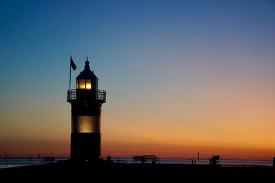 Silhouette lighthouse by sea against sky during sunset