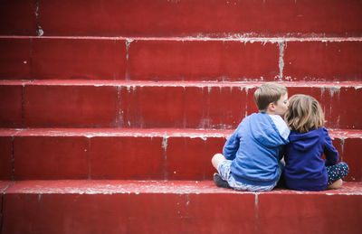 Rear view of boy kissing a girl and sitting against red wall