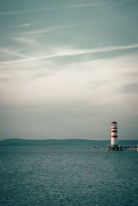 Lighthouse by sea against sky during sunset