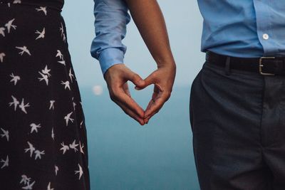 Midsection of couple holding heart shape hands